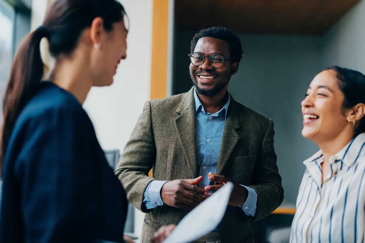 Three diverse business professionals smiling and talking together during an informal meeting in a modern office